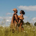 Wedding couple walking in a field with flowers and blue sky.
