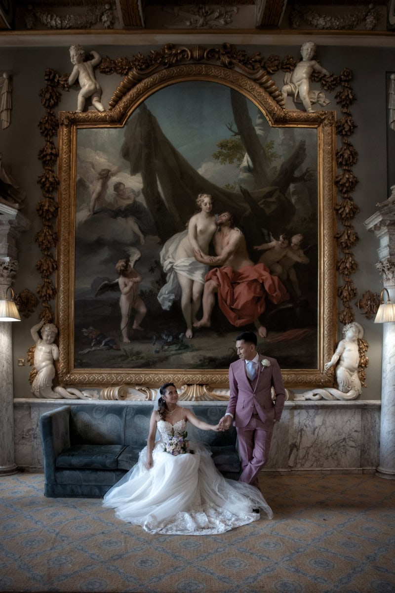 Wedding couple holding hands in grand historic interior setting.